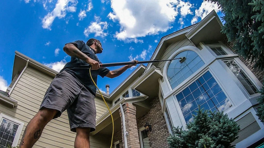 A boy is cleaning the window outside the house.